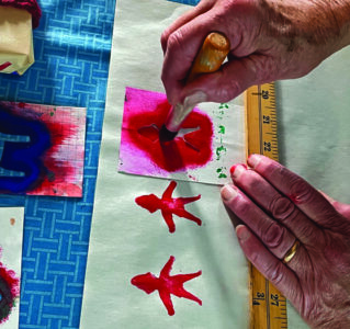 a hand holding a standing person stencil along a ruler and coloring it red.